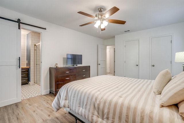 bedroom featuring connected bathroom, a barn door, light wood-style floors, visible vents, and baseboards
