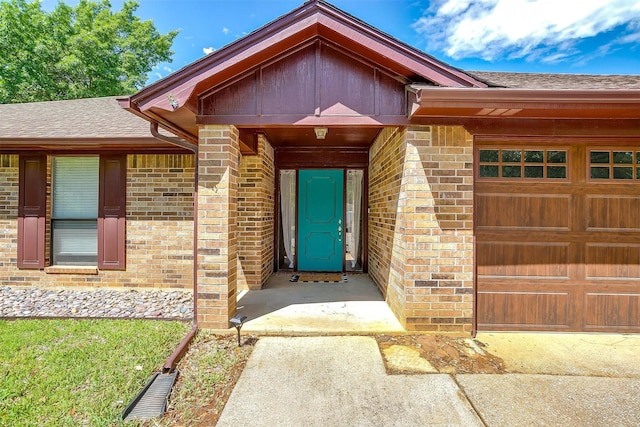 view of exterior entry featuring a shingled roof, brick siding, and a garage