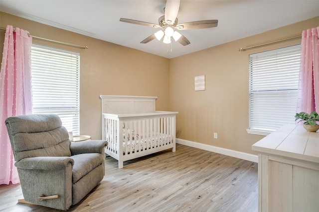 bedroom with light wood-type flooring, baseboards, a nursery area, and multiple windows