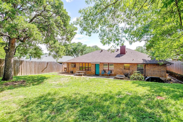 back of house with a patio, a chimney, a yard, brick siding, and a fenced backyard