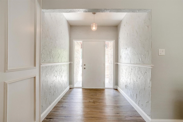 foyer with wood finished floors, a textured wall, and baseboards