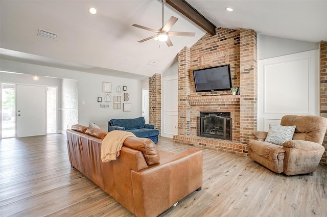 living room with vaulted ceiling with beams, light wood-style flooring, a fireplace, visible vents, and a ceiling fan