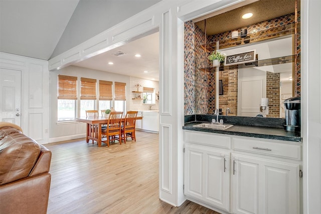 bar featuring vaulted ceiling, light wood finished floors, a sink, wet bar, and visible vents