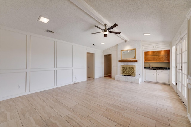unfurnished living room with vaulted ceiling with beams, a decorative wall, visible vents, a ceiling fan, and a textured ceiling