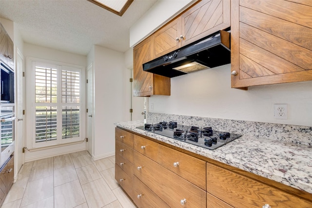 kitchen with black gas cooktop, brown cabinets, baseboards, and under cabinet range hood