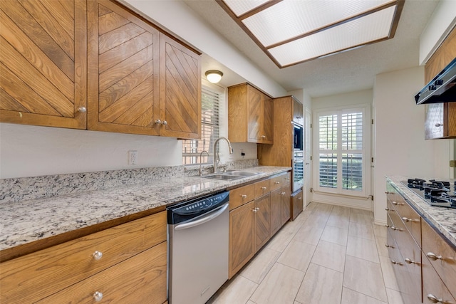 kitchen with brown cabinetry, a sink, light stone counters, and stainless steel appliances