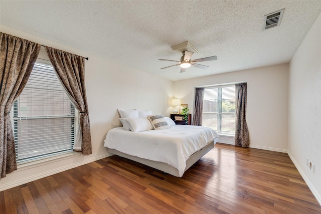bedroom with wood finished floors, visible vents, a ceiling fan, and a textured ceiling