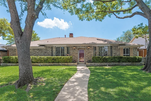 ranch-style home with roof with shingles, a chimney, a front yard, and brick siding