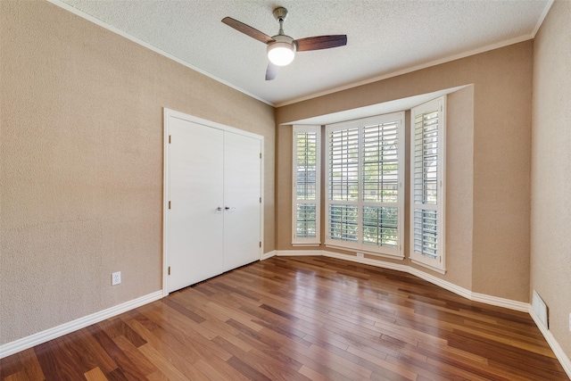 unfurnished bedroom featuring baseboards, wood finished floors, ornamental molding, and a textured wall