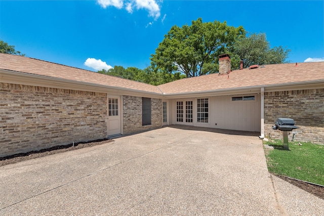 back of house with a chimney, brick siding, french doors, and a patio area