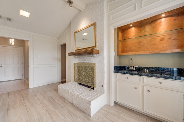 interior space featuring vaulted ceiling with beams, light tile patterned floors, a brick fireplace, wet bar, and visible vents