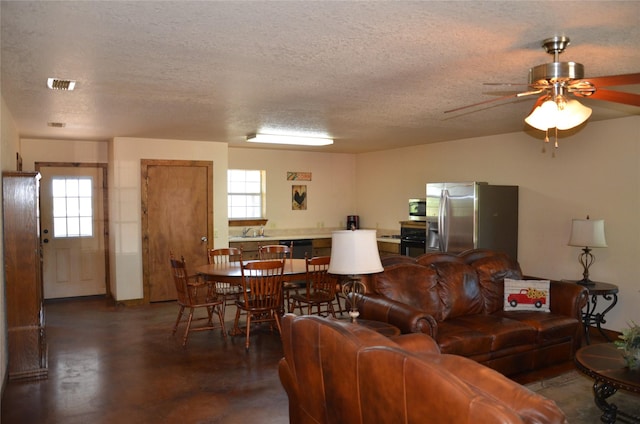 living room featuring finished concrete flooring, a textured ceiling, visible vents, and a ceiling fan