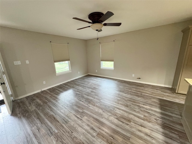 spare room featuring a ceiling fan, baseboards, wood finished floors, and a healthy amount of sunlight