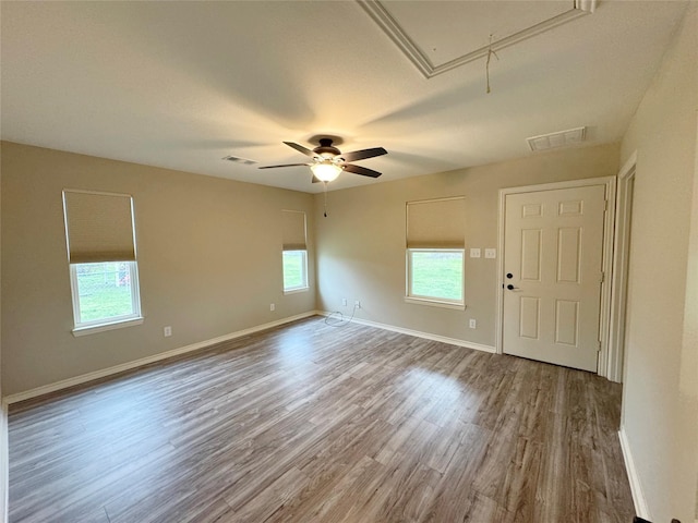 empty room with attic access, a ceiling fan, visible vents, baseboards, and wood finished floors