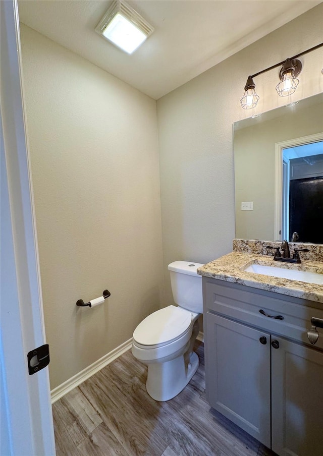 half bath with baseboards, wood finished floors, toilet, and vanity