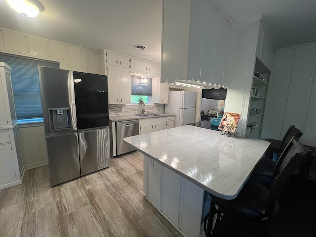 kitchen with a decorative wall, appliances with stainless steel finishes, white cabinetry, and a sink