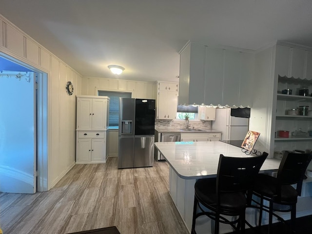 kitchen featuring light wood-style flooring, stainless steel appliances, light countertops, a sink, and white cabinetry