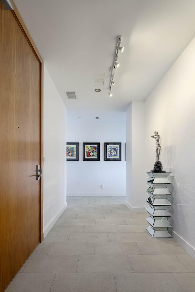 hallway with rail lighting, light tile patterned flooring, visible vents, and baseboards
