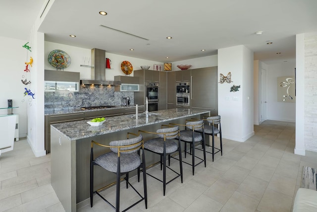 kitchen featuring a kitchen breakfast bar, tasteful backsplash, island range hood, stainless steel double oven, and a large island with sink