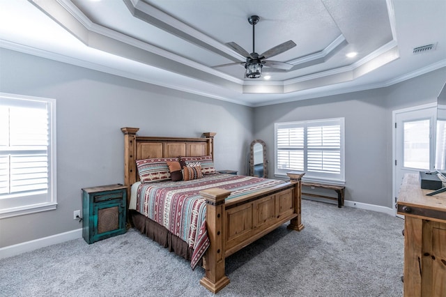 carpeted bedroom with crown molding, visible vents, a tray ceiling, baseboards, and a ceiling fan