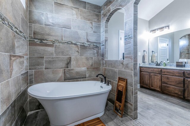 full bath featuring a soaking tub, vaulted ceiling, tile walls, wood finished floors, and vanity
