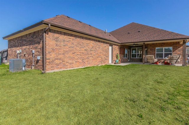 rear view of house featuring central air condition unit, a shingled roof, a patio area, a yard, and brick siding