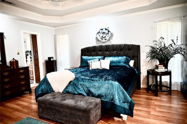 bedroom featuring visible vents, wood finished floors, crown molding, and a tray ceiling