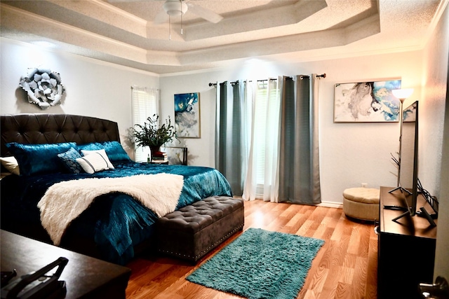 bedroom with wood finished floors, a raised ceiling, and ornamental molding