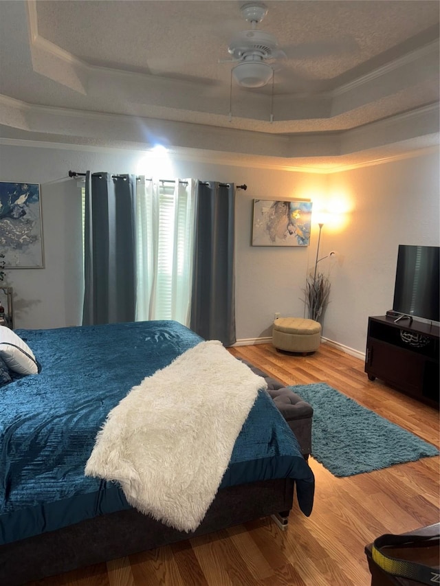 bedroom with wood finished floors, a ceiling fan, a tray ceiling, and baseboards