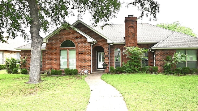 view of front facade with a front lawn, a shingled roof, a chimney, and brick siding