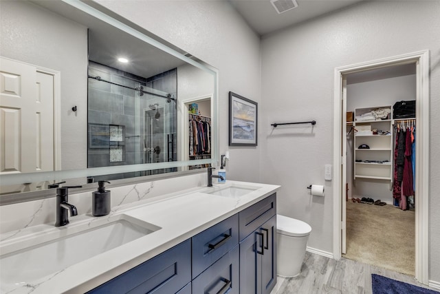 bathroom with a sink, a shower stall, double vanity, visible vents, and wood finished floors