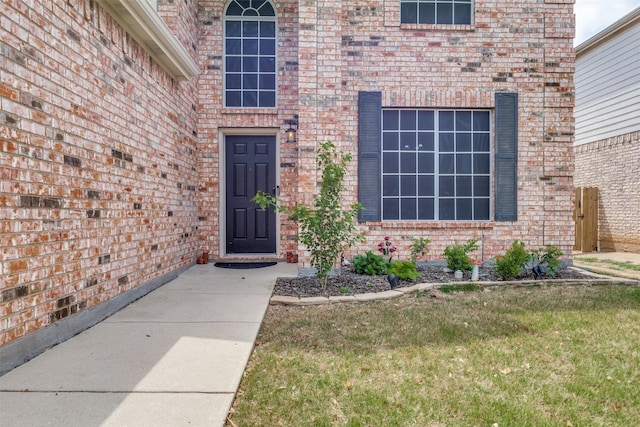 view of exterior entry featuring a yard and brick siding