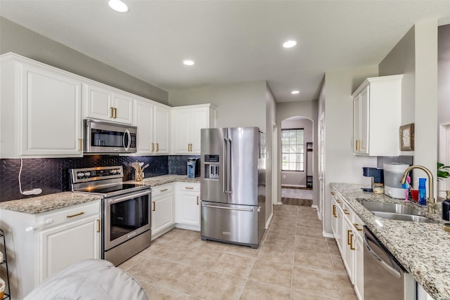 kitchen featuring a sink, decorative backsplash, white cabinetry, arched walkways, and appliances with stainless steel finishes