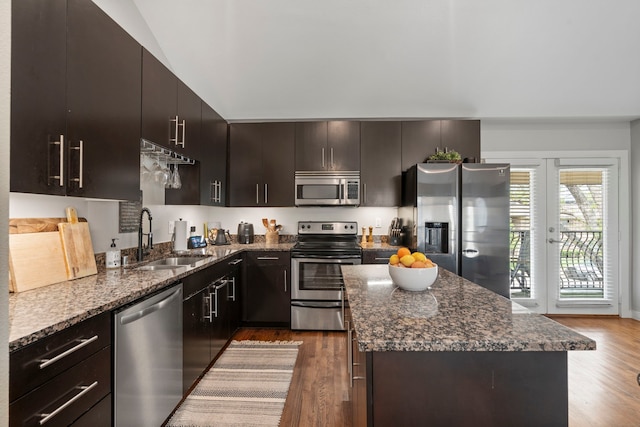 kitchen featuring dark stone counters, wood finished floors, stainless steel appliances, and a sink