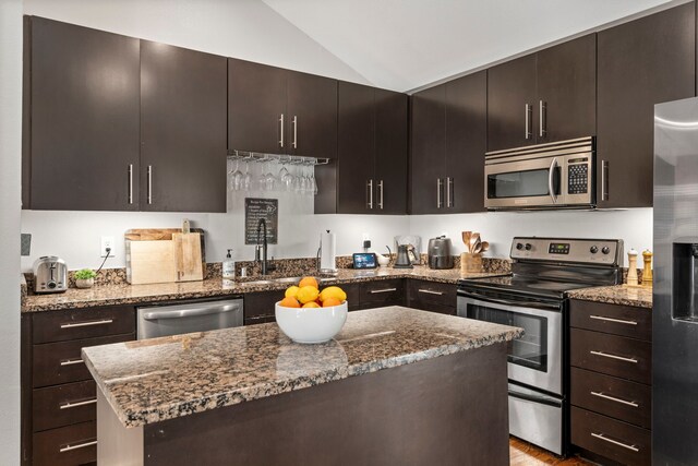 kitchen with dark stone countertops, appliances with stainless steel finishes, a kitchen island, a sink, and lofted ceiling