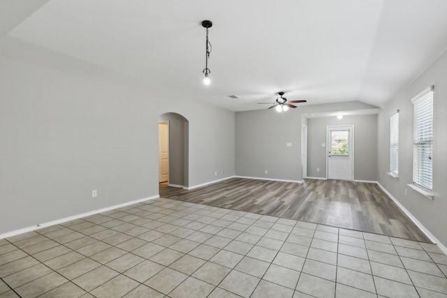 unfurnished living room featuring light wood-style floors, baseboards, arched walkways, vaulted ceiling, and a ceiling fan