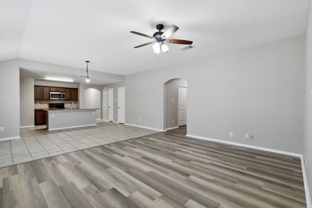 unfurnished living room with a ceiling fan, visible vents, light wood-style flooring, baseboards, and arched walkways