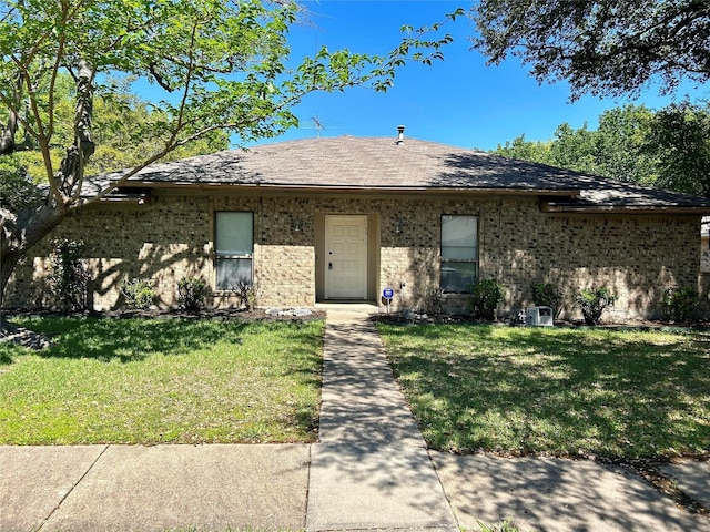 view of front of house with a front yard, a shingled roof, and brick siding
