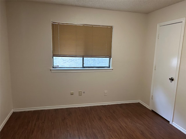 spare room with baseboards, a textured ceiling, and dark wood-type flooring