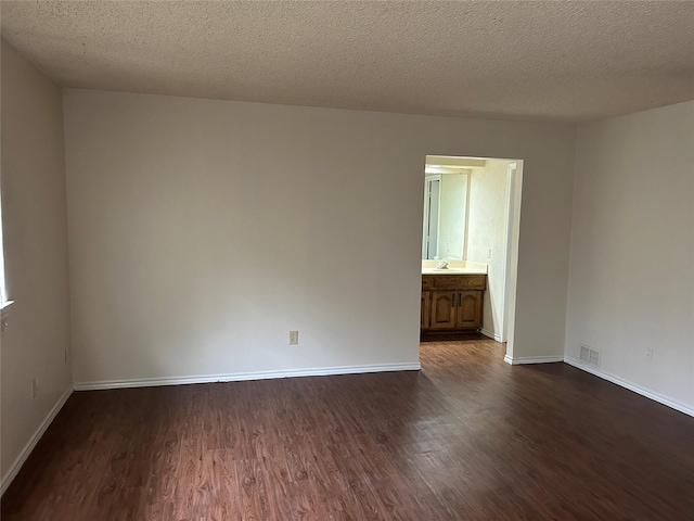 spare room with a textured ceiling, a sink, visible vents, dark wood-style floors, and baseboards