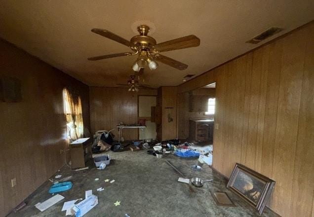 empty room with visible vents, a ceiling fan, and wooden walls