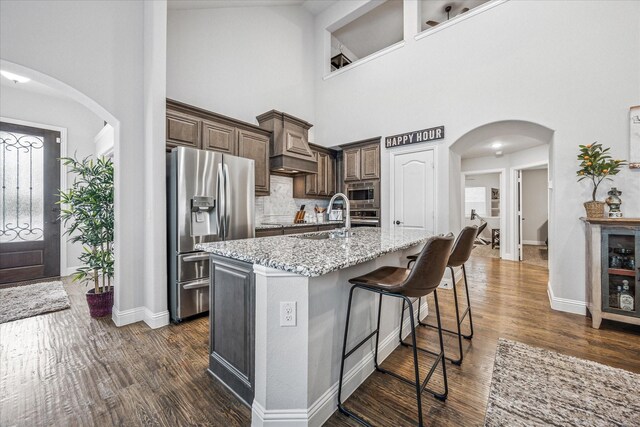 kitchen featuring a sink, appliances with stainless steel finishes, arched walkways, dark wood-style flooring, and a towering ceiling