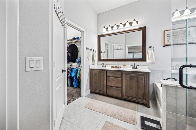 full bathroom featuring tile patterned flooring, double vanity, a walk in closet, a stall shower, and a garden tub