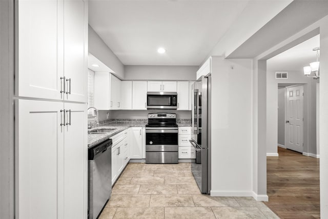 kitchen featuring a sink, light stone counters, stainless steel appliances, and white cabinetry