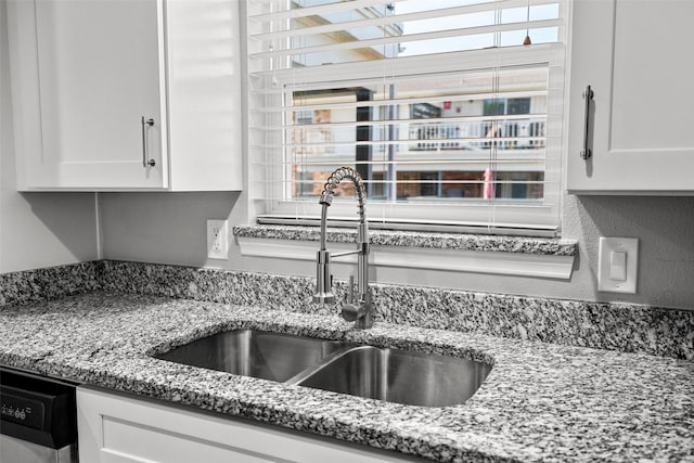 kitchen with white cabinets, light stone counters, dishwasher, and a sink