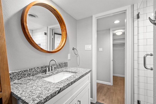 full bath with a shower stall, vanity, a walk in closet, baseboards, and wood finished floors