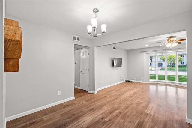 empty room featuring ceiling fan with notable chandelier, visible vents, wood finished floors, and baseboards