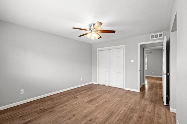 unfurnished bedroom featuring a closet, a ceiling fan, visible vents, baseboards, and wood finished floors