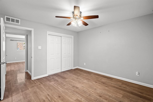 unfurnished bedroom featuring wood finished floors, a closet, ceiling fan, baseboards, and visible vents
