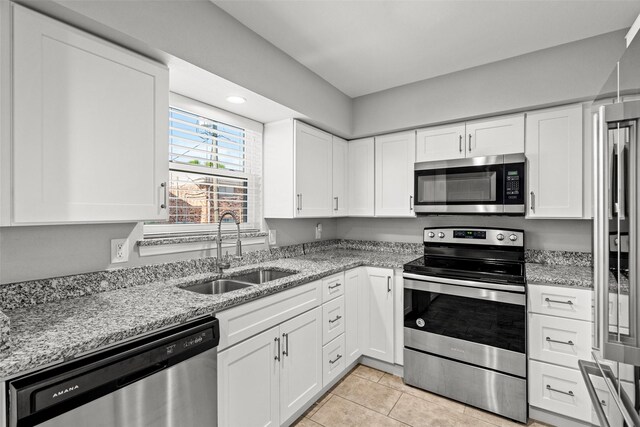 kitchen with light stone countertops, a sink, white cabinets, and stainless steel appliances